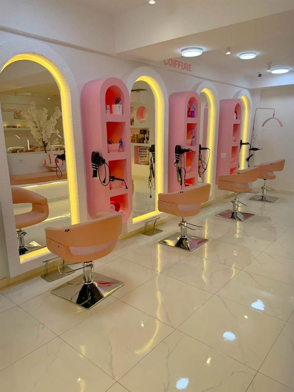 Les postes de coiffure de Maison Bulma : arches roses rétroéclairées, miroirs et fauteuils pêche